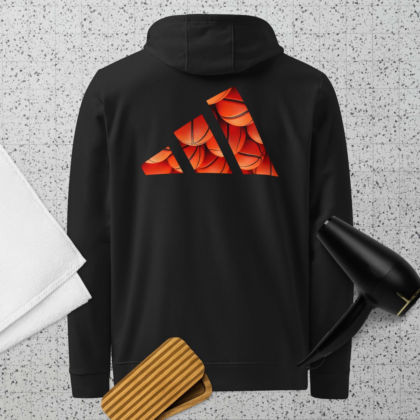Vista trasera de la sudadera negra con capucha y manga larga de la colección Adidas de Bofetadas. En la parte posterior, las tres barras del logotipo de Adidas están rellenas con balones de baloncesto apilados.