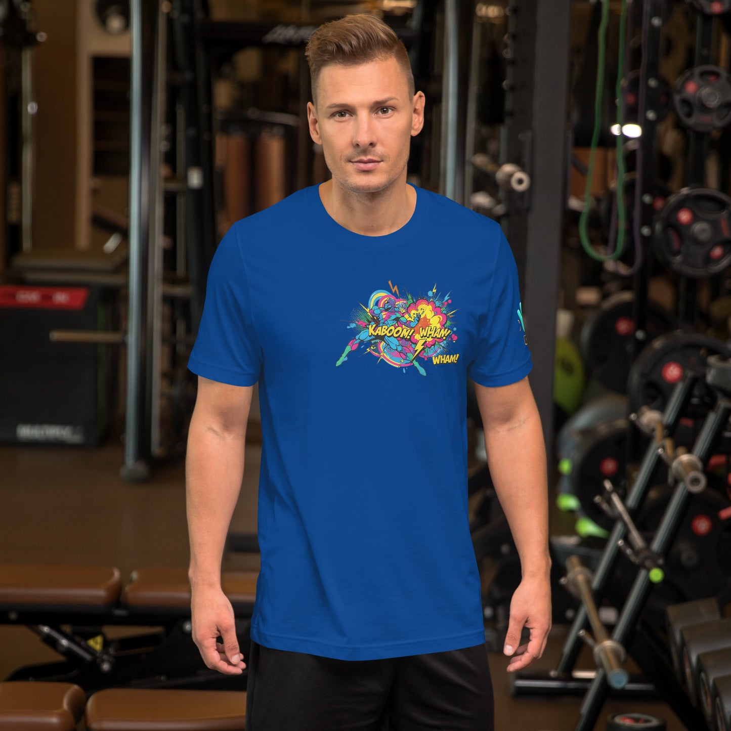 Modelo en gimnasio luciendo camiseta azul de manga corta marca Bofetadas, colección 'Pop', con imagen colorida de cómic, de un superhéroe en acción, explosión, rayos y textos 'kaboom', 'wham'.