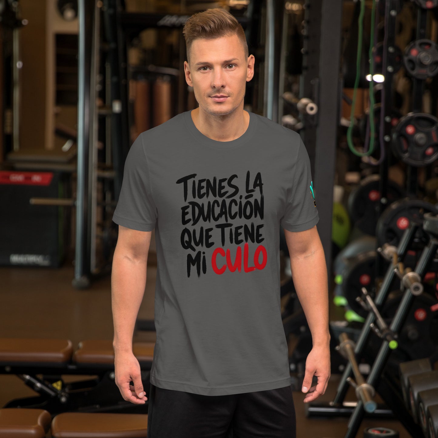 Modelo en gimnasio luciendo camiseta gris de manga corta marca Bofetadas, colección 'Irreverentes', con texto 'tienes la educación que tiene mi' en negro y 'culo' en rojo.