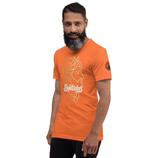 Un modelo con barba y pelo corto luce una camiseta naranja de Bofetadas de la colección Asesinos en serio. Tiene impreso en el frente una ilustración lineal de el rostro de Alejandro Magno y la tipografía de Bofetadas. Se aprecia en la manga izquierda el logotipo de la nueva colección.