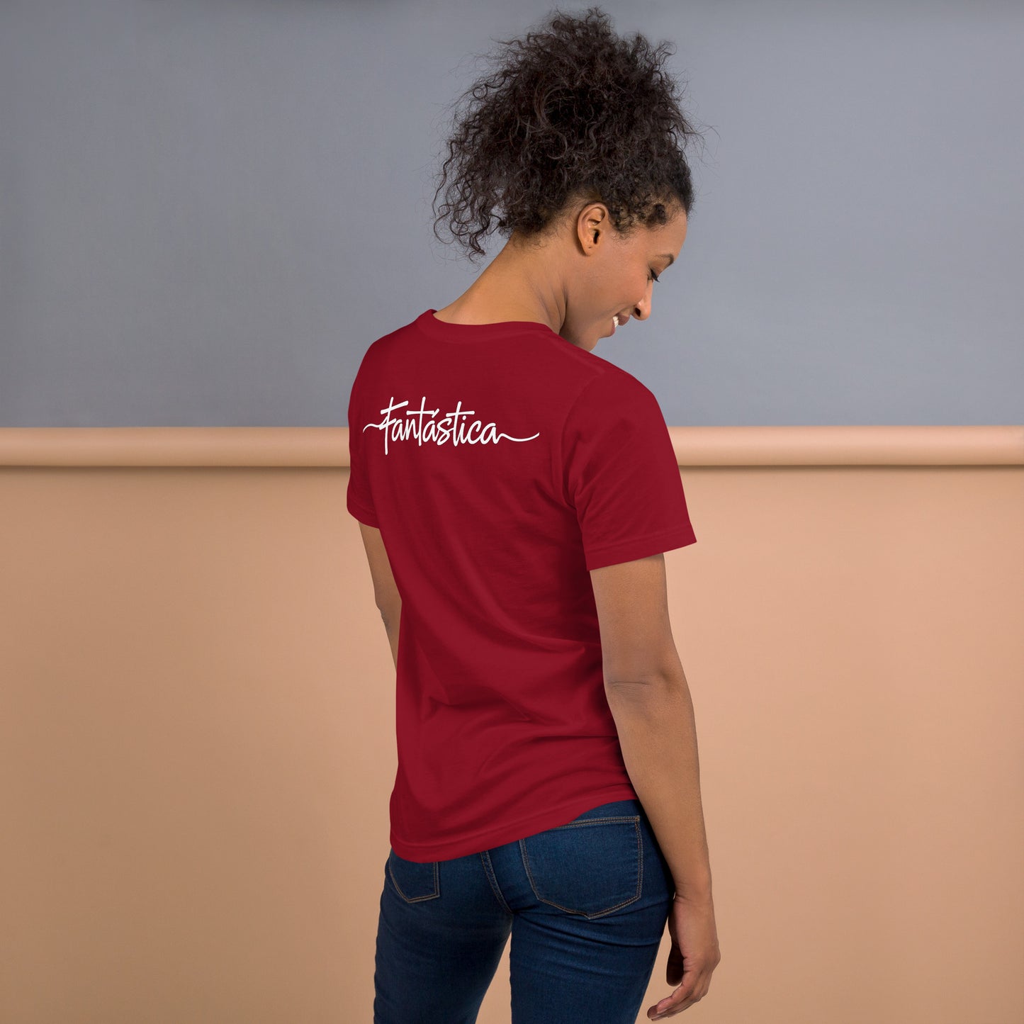 Modelo sonriente con pelo recogido y vaqueros luce la camiseta roja de la colección 'Calaveras', vista trasera, con la palabra 'Fantástica' impresa en la espalda.