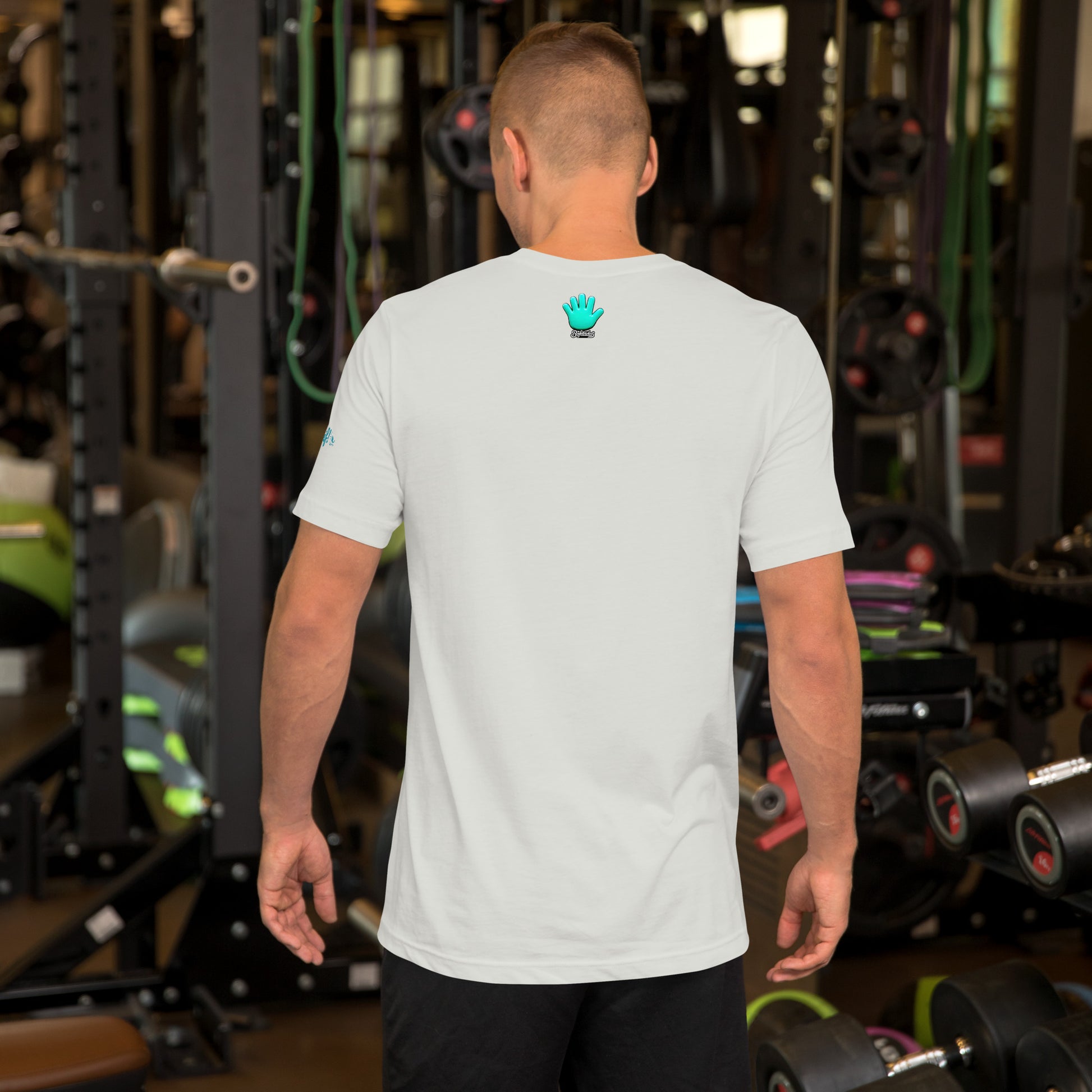 Un modelo en un gimnasio nos enseña la vista trasera de la camiseta blanca de la colección Emo que tiene la impresión del logo de Bofetadas con la mano azul en pequeñito y en el centro de la parte superior de la espalda.