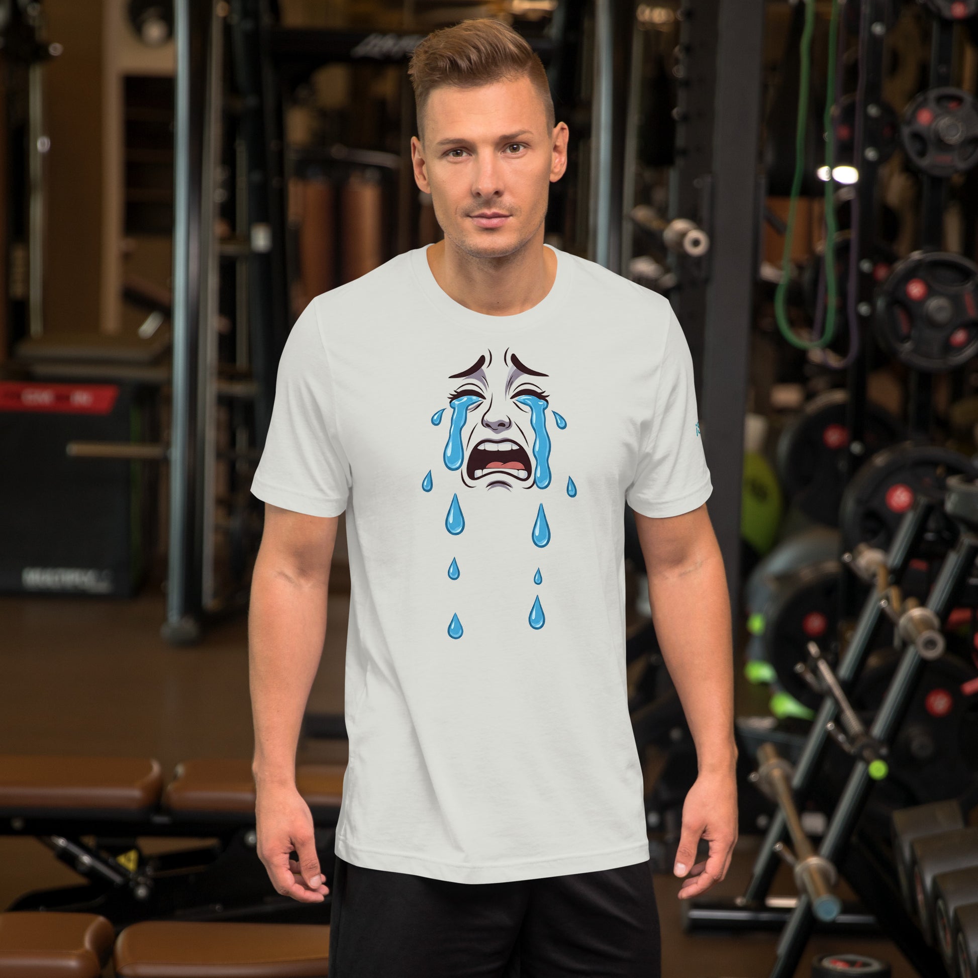 Un modelo en un gimnasio nos muestra la vista frontal de la camiseta blanca de la colección Emo con la impresión de un dibujo de una mueca triste llorando desconsoladamente, con unas lágrimas.