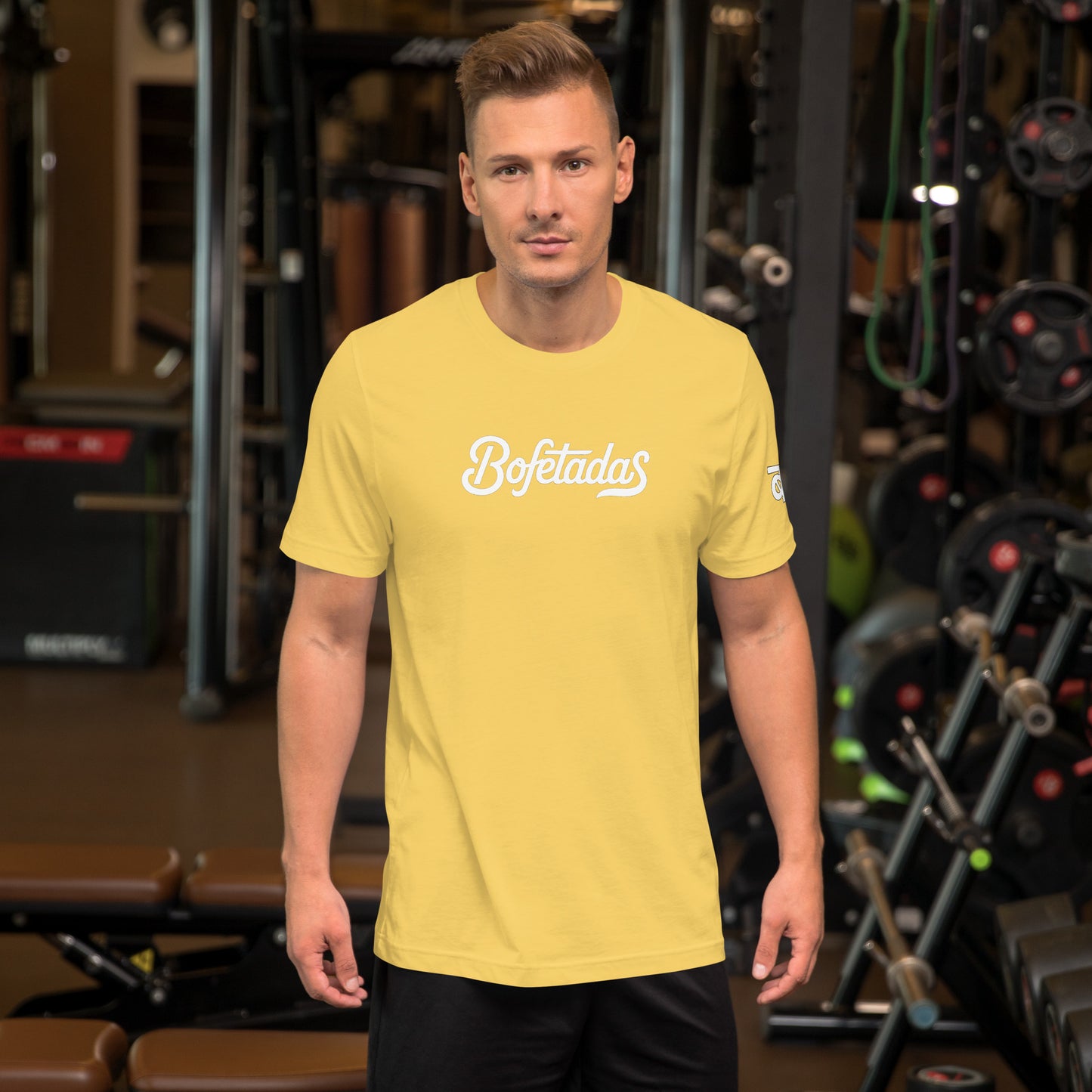 Vista frontal de la camiseta amarilla de la colección 'Marca' de Bofetadas, la luce un modelo en el gimnasio, con el nombre de la marca impreso en el pecho en tipografía blanca.