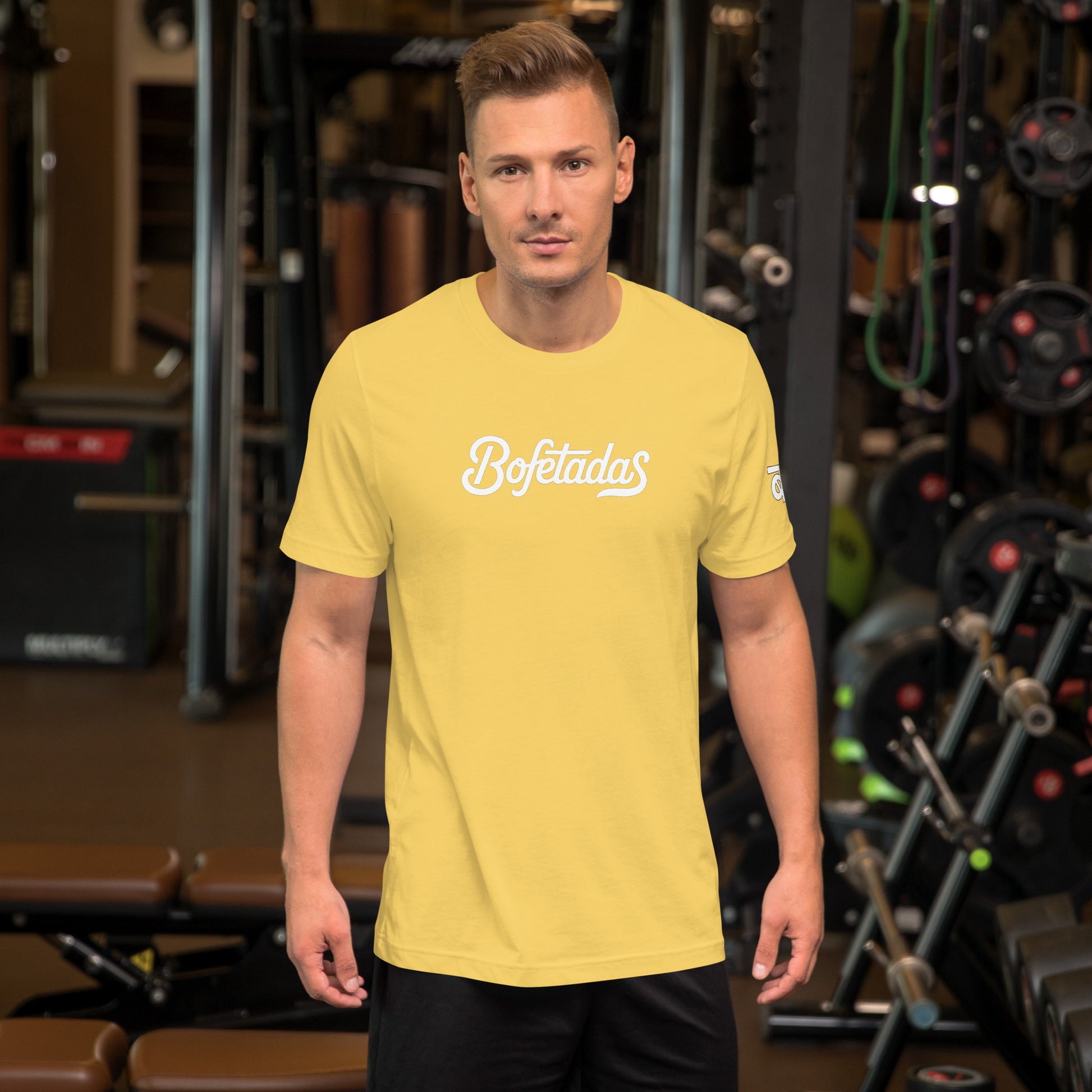 Vista frontal de la camiseta amarilla de la colección 'Marca' de Bofetadas, la luce un modelo en el gimnasio, con el nombre de la marca impreso en el pecho en tipografía blanca.