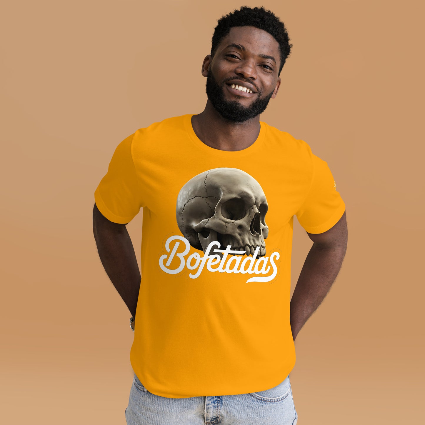 Un modelo luce en un  estudio la camiseta amarilla de manga corta marca Bofetadas, colección 'Calaveras', con una calavera sin mandíbula inferior en la impresión encima del texto "Bofetadas".