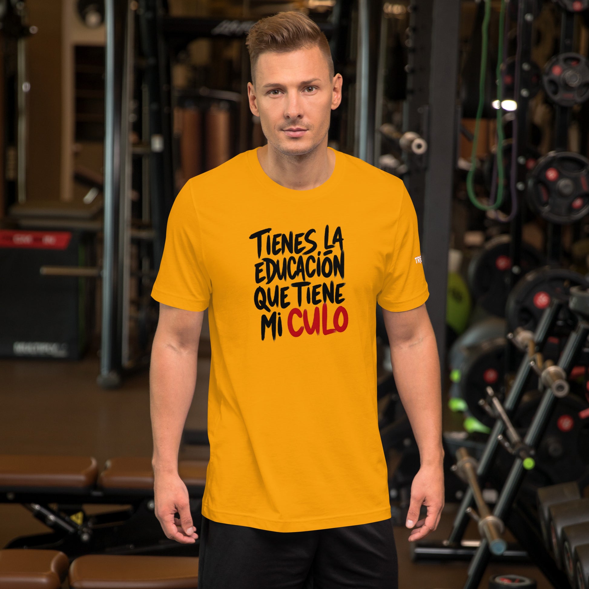 Modelo en gimnasio luciendo camiseta amarilla de manga corta marca Bofetadas, colección 'Irreverentes', con texto 'tienes la educación que tiene mi' en negro y 'culo' en rojo. Y la palabra TREMENDA en la manga izquierda.