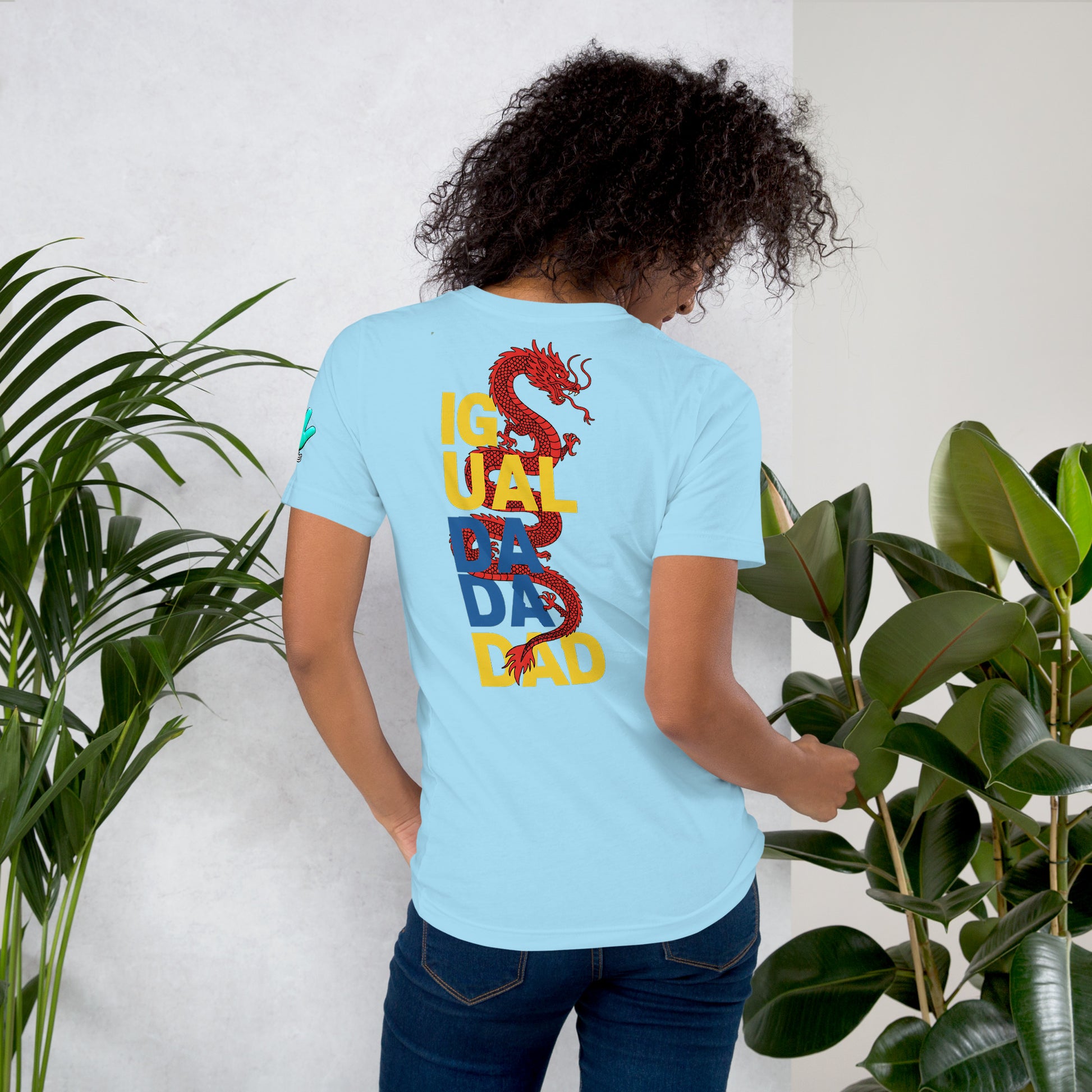 Una modelo mostrando la vista trasera de camiseta azul claro de manga corta, marca Bofetadas, colección 'Causas Sociales', con la impresión del texto en cuatro filas "IGUAL-DA-DA-DAD" y un dragón rojo enrollado en ellas.