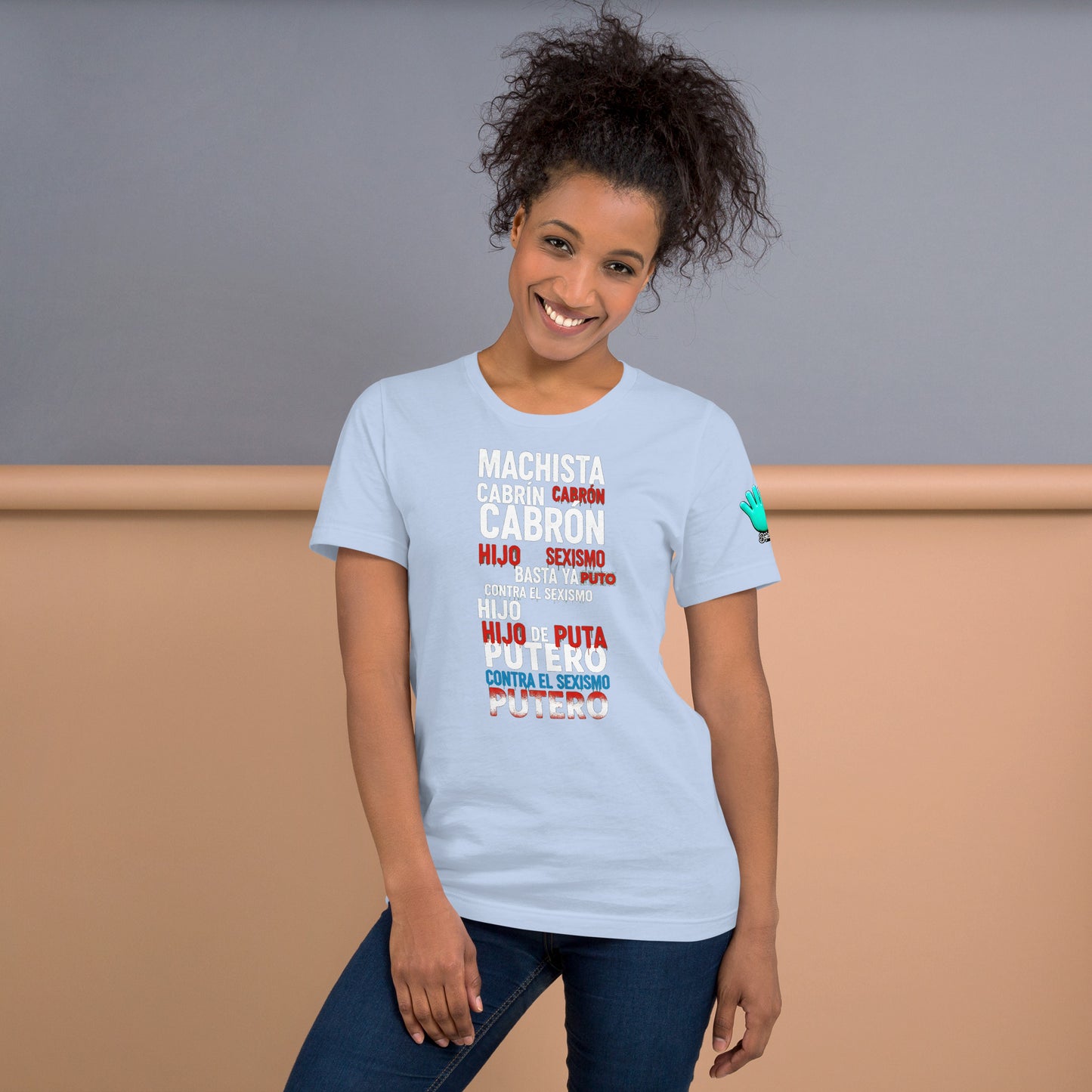 Una modelo sonriente en jeans mostrando la vista delantera de una camiseta azul claro de manga corta, marca Bofetadas, colección 'Causas Sociales', la impresión de un mensaje o cartel de protesta anti-sexista, agresivo y con carga política, que utiliza un lenguaje contundente. El texto en blanco, azul y rojo.