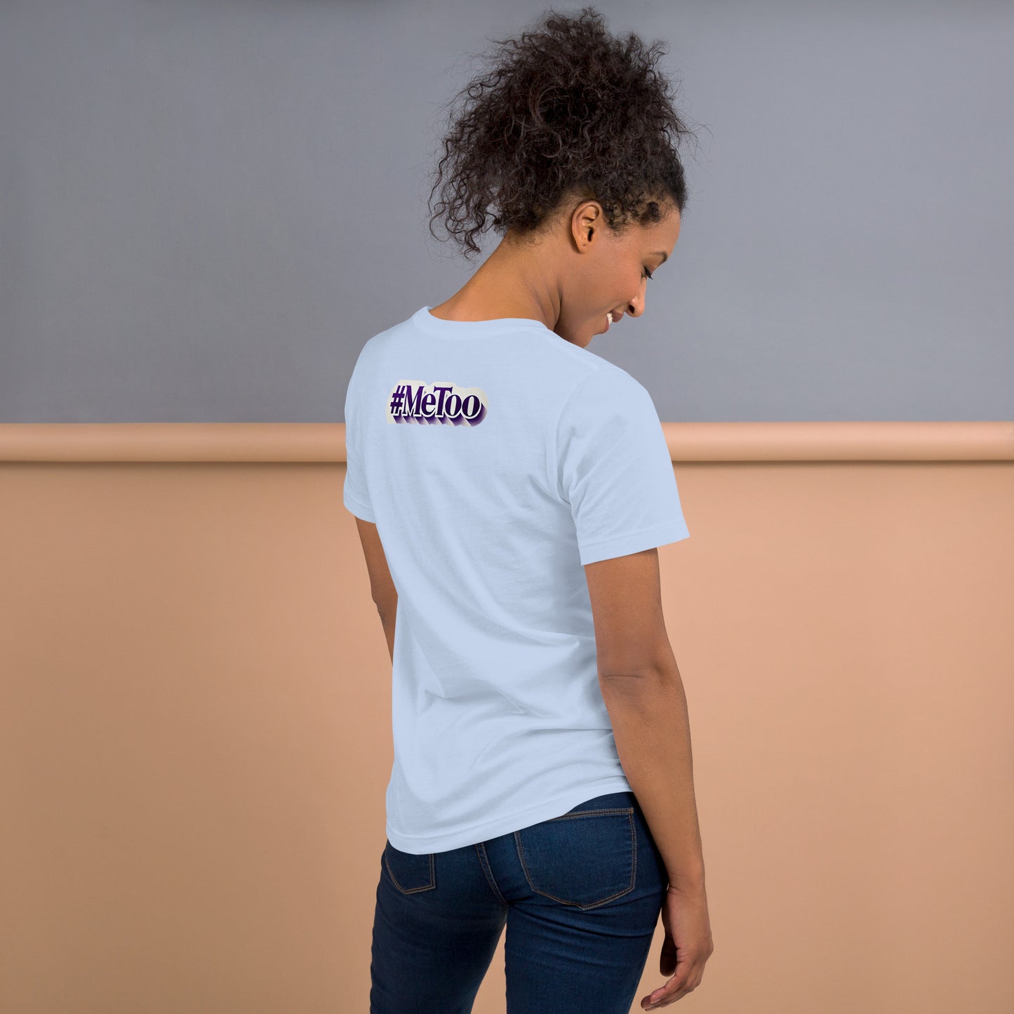 Una modelo sonriente en jeans mostrando la vista trasera de una camiseta azul claro de manga corta, marca Bofetadas, colección 'Causas Sociales', la impresión del mensaje texto '#metoo' en letras lilas con borde blanco y sombra.