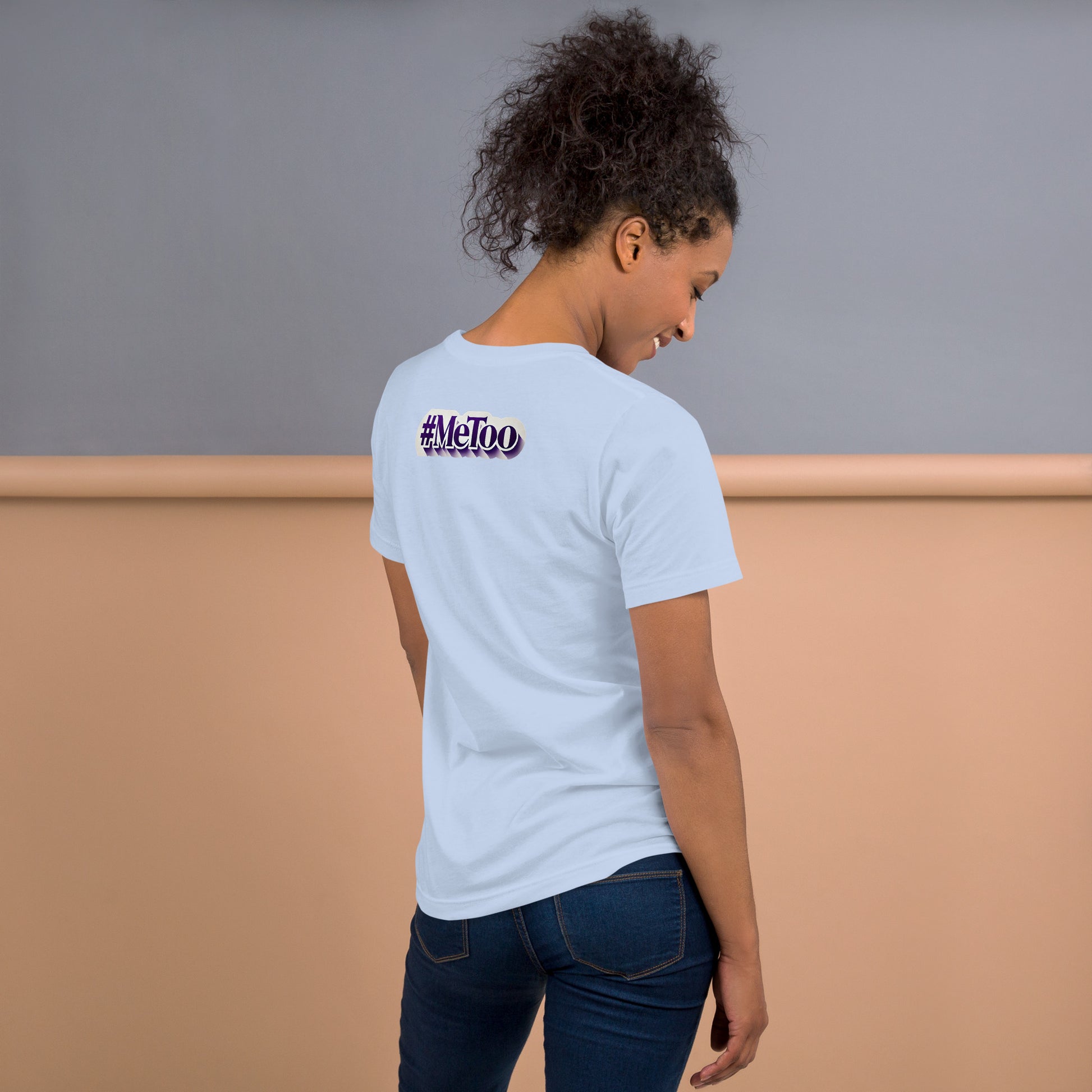 Una modelo sonriente en jeans mostrando la vista trasera de una camiseta azul claro de manga corta, marca Bofetadas, colección 'Causas Sociales', la impresión del mensaje texto '#metoo' en letras lilas con borde blanco y sombra.