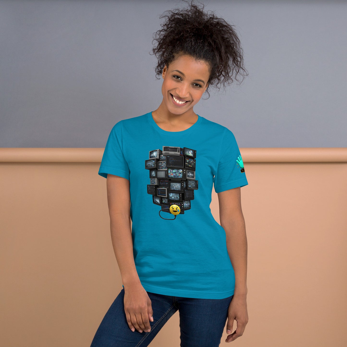 Una modelo sonriente con pelo recogido y jeans luciendo camiseta azul de manga corta marca Bofetadas, colección 'Emojis', vista frontal, con emoji sudando conectado a TVs apiladas.