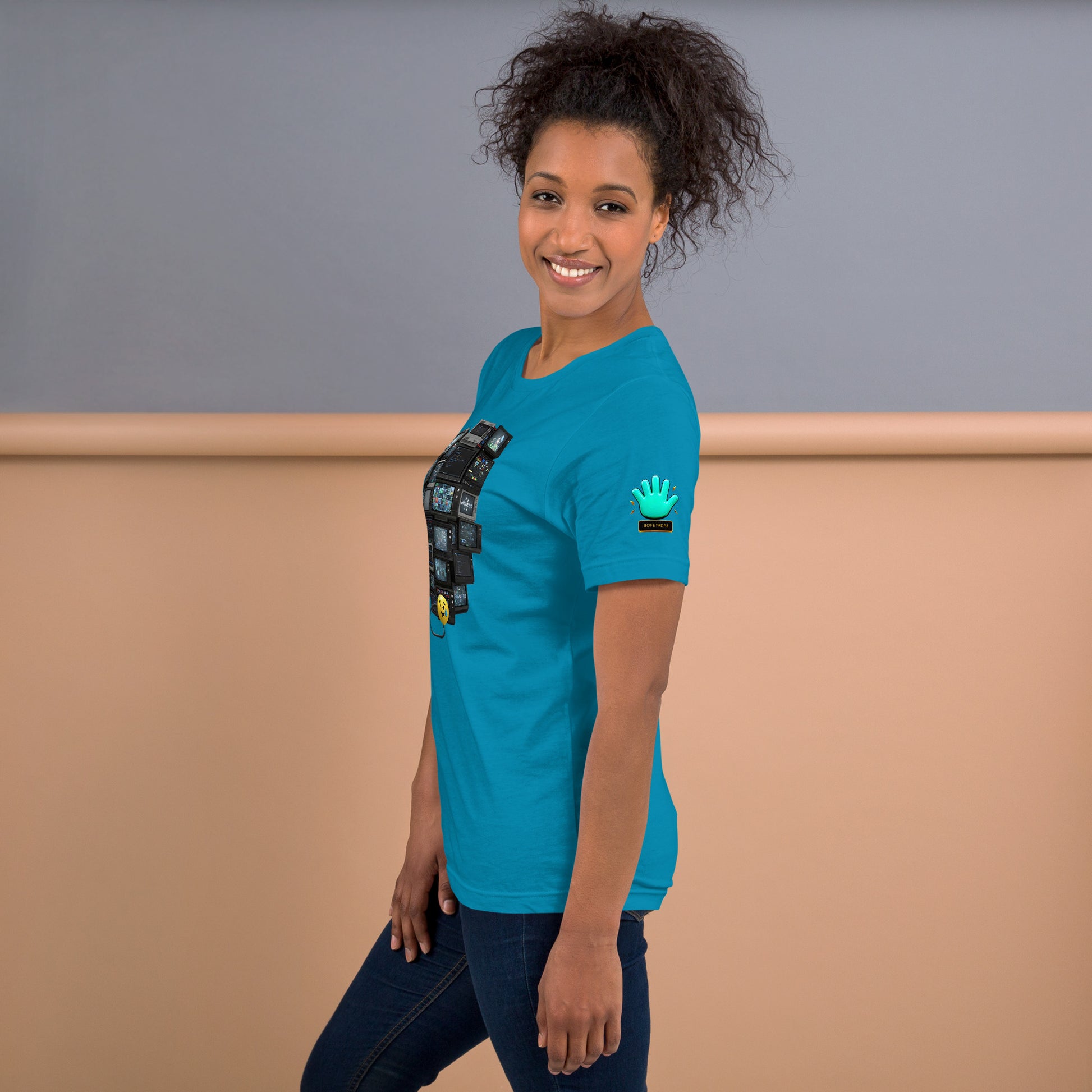 Una modelo  sonriente con pelo recogido y jeans mostrando la vista lateral de camiseta azul de manga corta, marca Bofetadas, colección 'Emojis', con el logotipo de una mano azul en la manga.