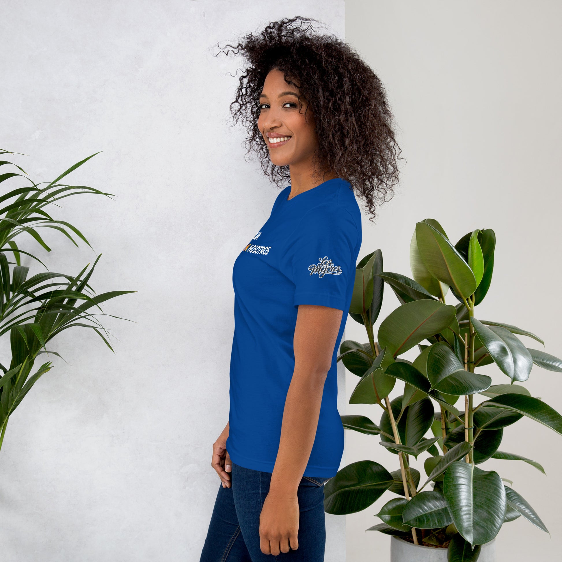 Modelo sonriente con pelo suelto y jeans mostrando la vista lateral de camiseta azul de manga corta, marca Bofetadas, colección 'Marca', con el texto "Las mejores" en la manga.