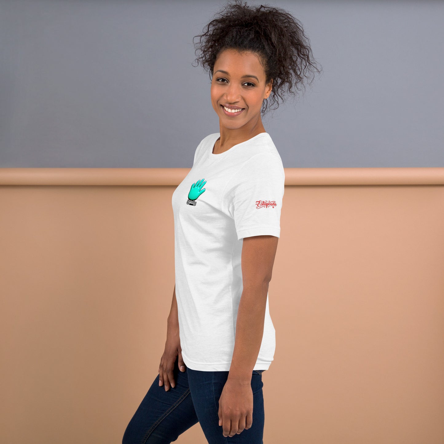 Una modelo con jeans sonríe vistiendo una camiseta blanca de manga corta marca Bofetadas, colección 'Calaveras', en la vista lateral se aprecia el logo de Bofetadas con la mano azul en el pecho y el texto Estupenda en la manga izquierda.