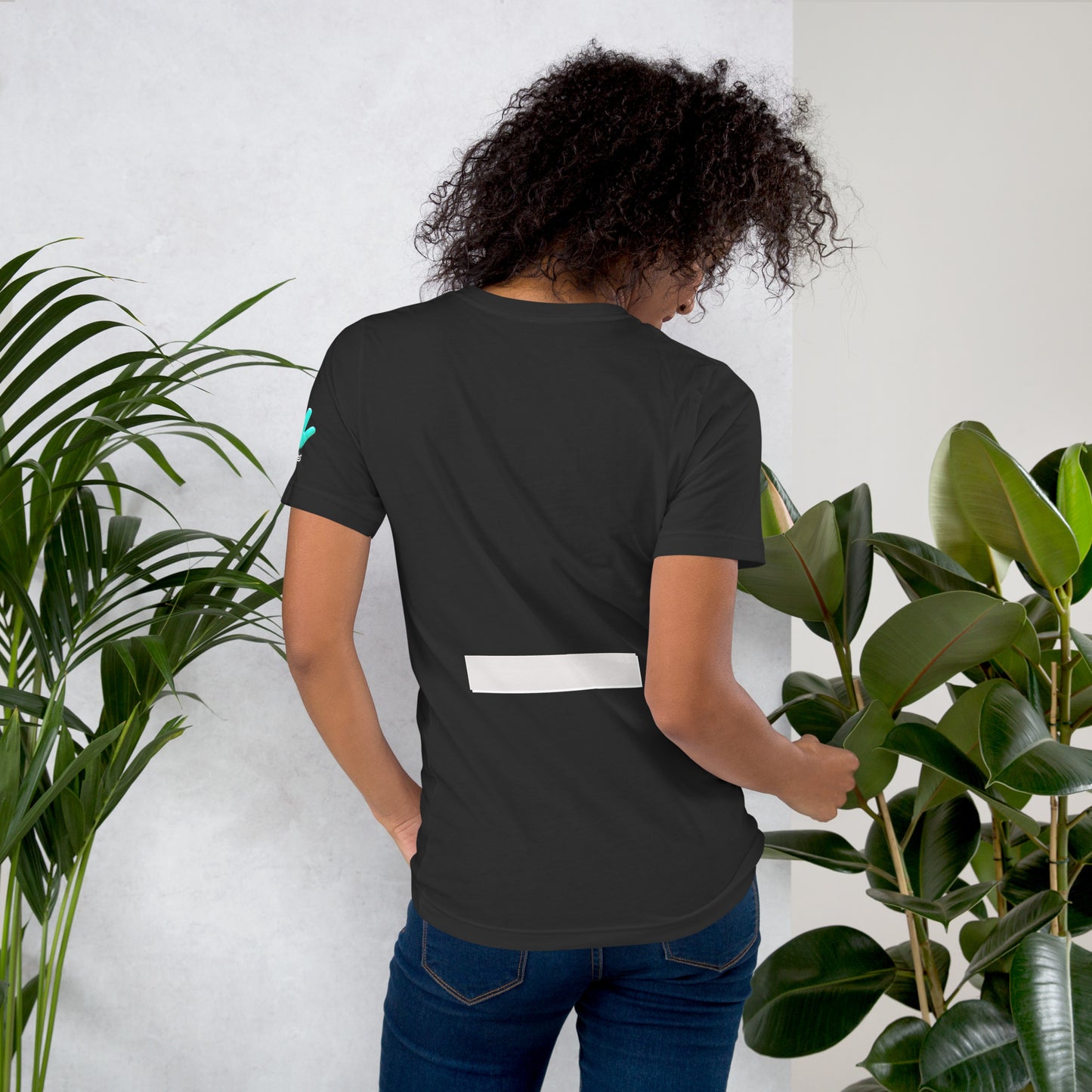 Modelo con jeans y un cabello voluminoso luce una camiseta gris oscuro de la colección Causas Sociales con la impresión en la zona lumbar de una raya horizontal que representa el signo menos.