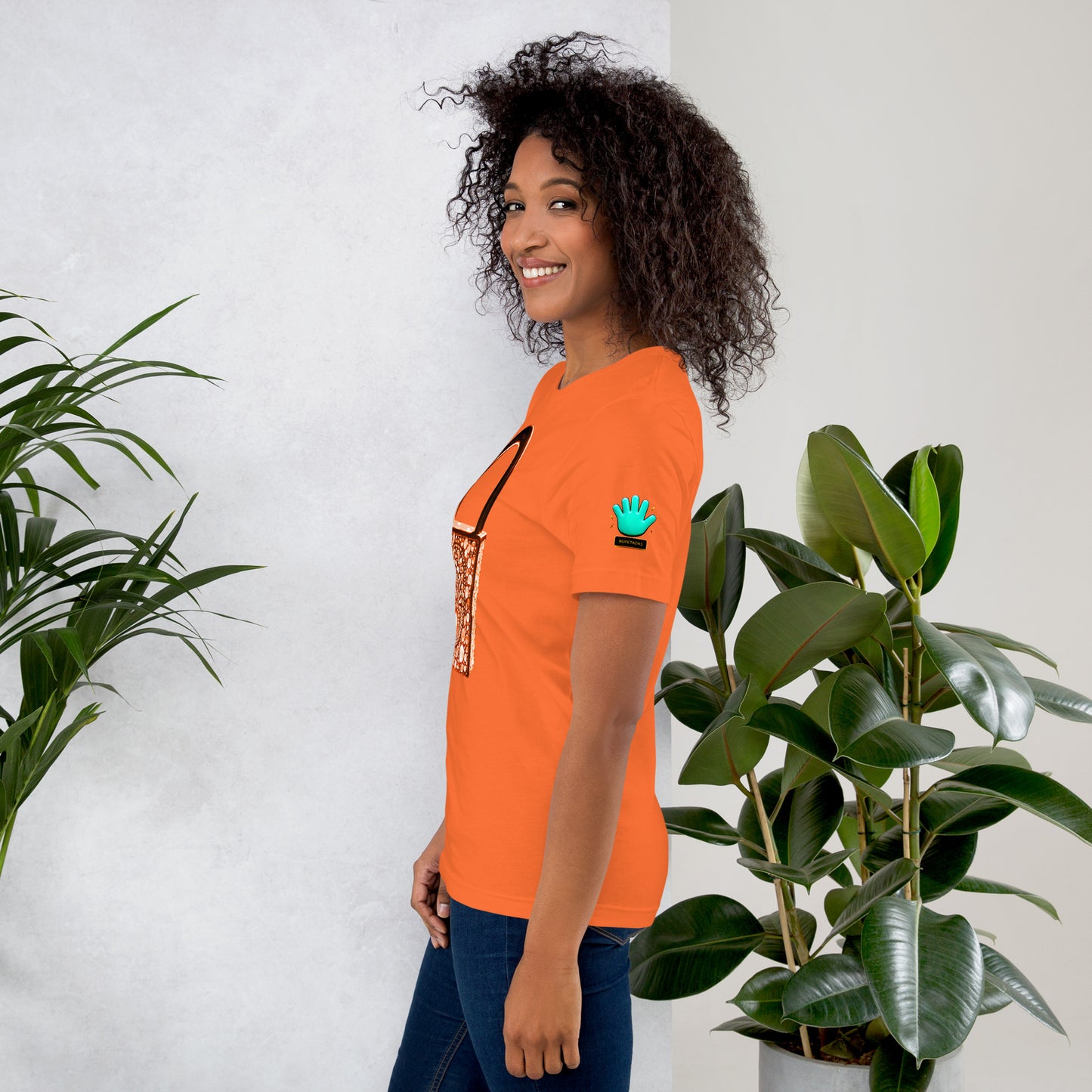Modelo con jeans y sonrisa mostrando la vista lateral de camiseta naranja de manga corta, marca Bofetadas, colección 'Símbolos', con el logotipo de una mano azul en la manga.