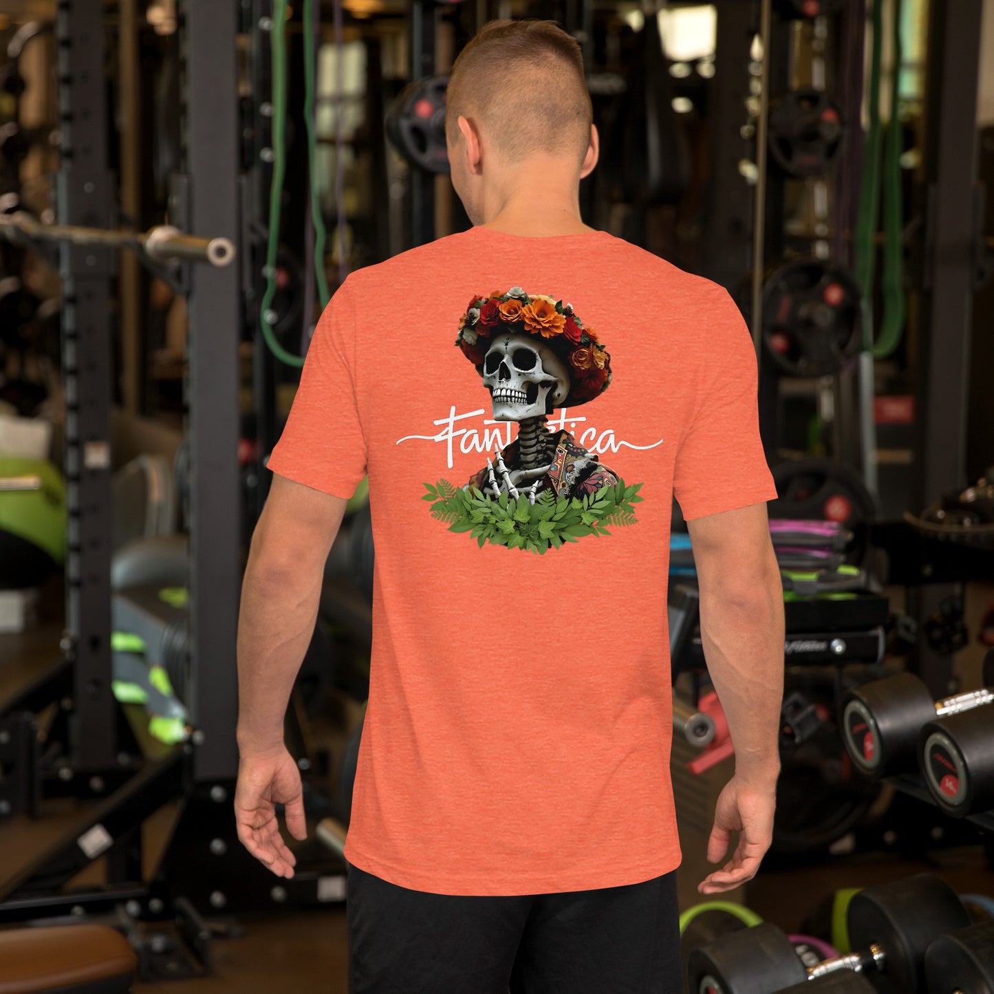 Modelo luciendo en un gimnasio la vista trasera de una camiseta naranja de manga corta marca Bofetadas, colección 'Calaveras', con esqueleto superior con calavera, chaqueta floral, corona de flores y marco inferior de hojas.
