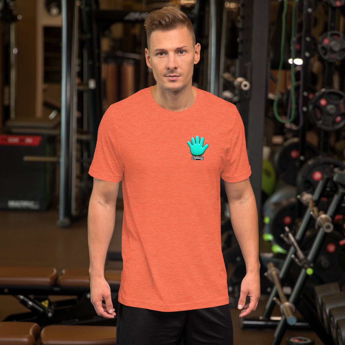 Modelo mostrando en gimnasio la vista frontal de una camiseta naranja de manga corta, marca Bofetadas, colección 'Calaveras', con el logotipo de una mano azul en la en el pecho.