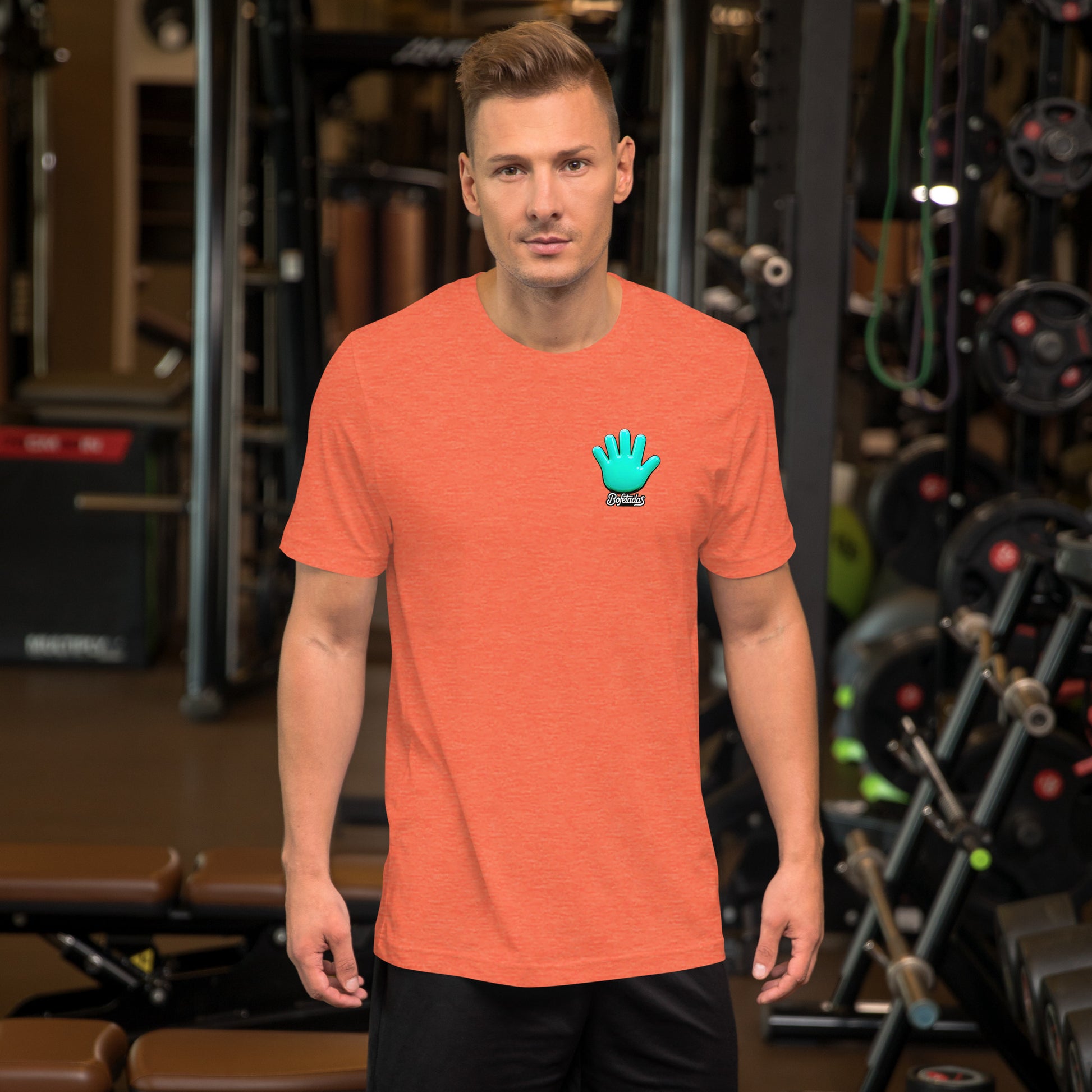 Modelo mostrando en gimnasio la vista frontal de una camiseta naranja de manga corta, marca Bofetadas, colección 'Calaveras', con el logotipo de una mano azul en la en el pecho.