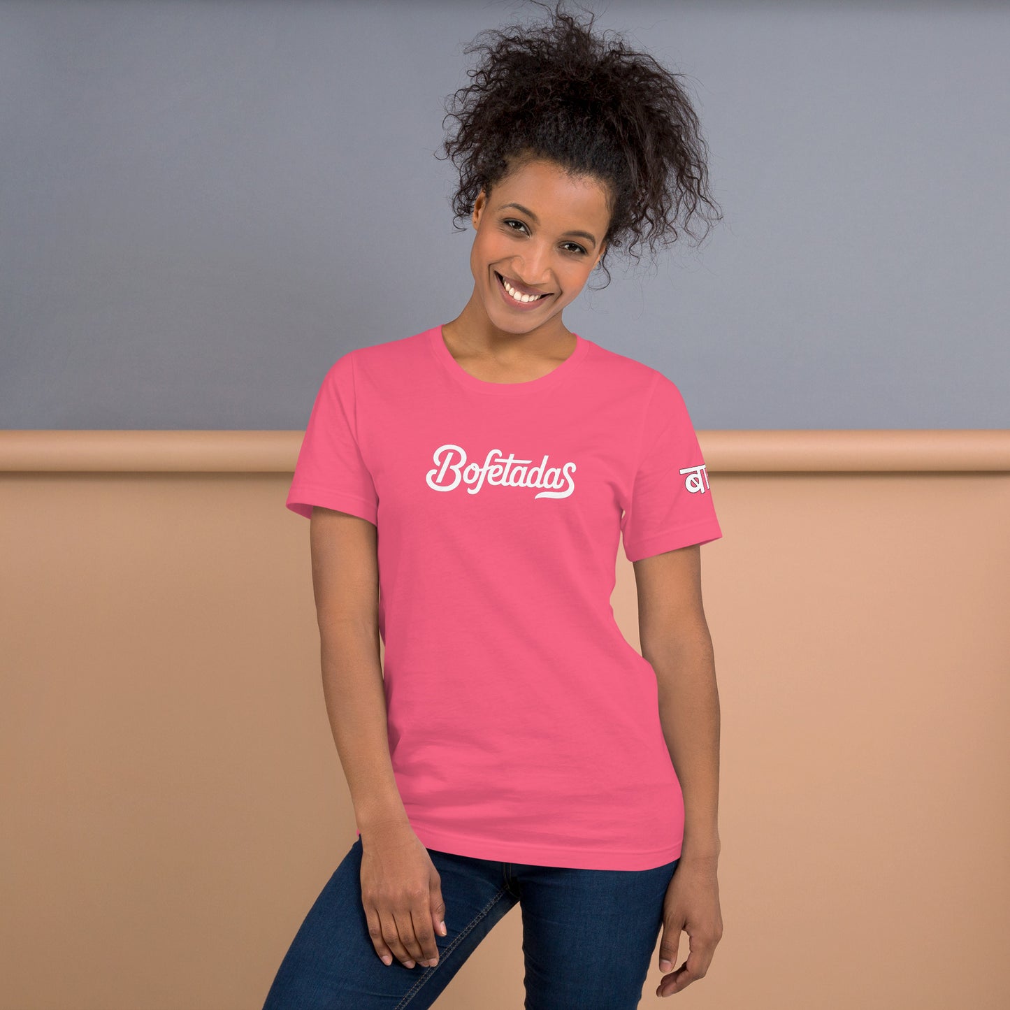 Vista frontal de la camiseta rosa de la colección 'Marca' de Bofetadas, con el nombre de la marca impreso en el pecho en tipografía blanca. La luce una modelo sonriente en jeans.