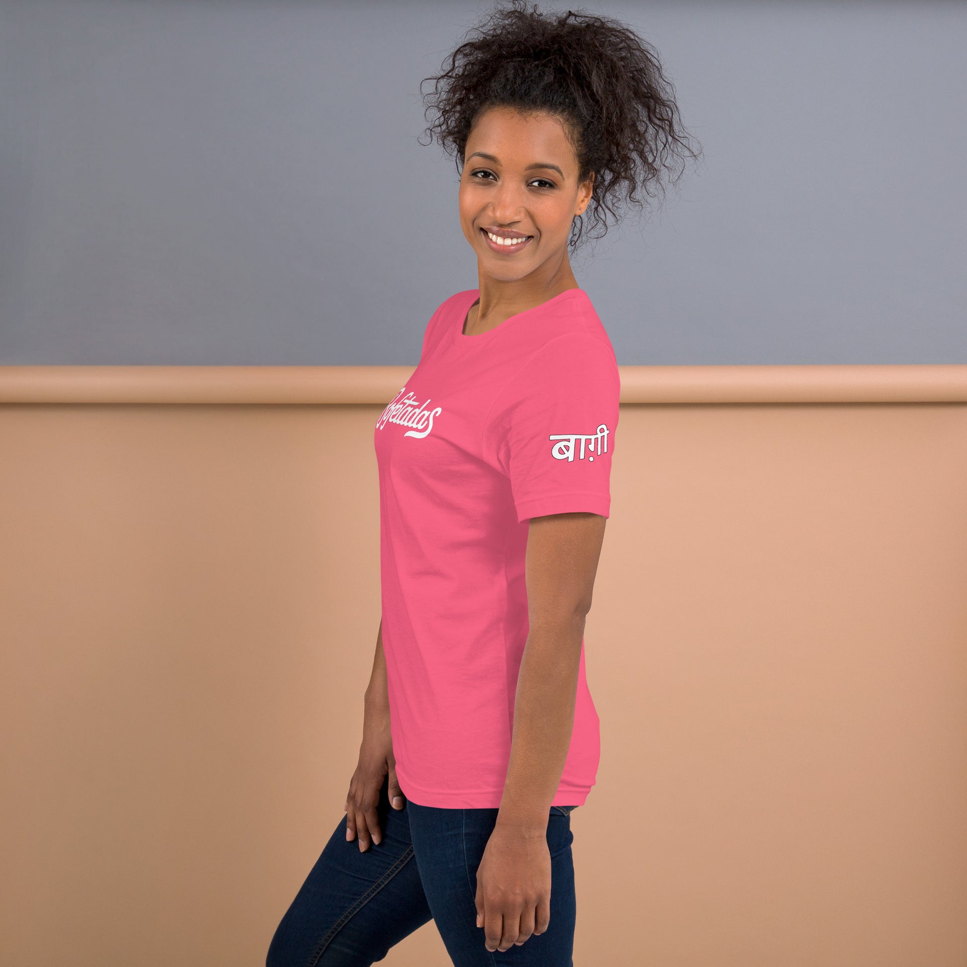 Camiseta color rosa de la colección 'Marca' con impresión en la manga del texto en indi "rebelde". La luce una modelo con jeans.